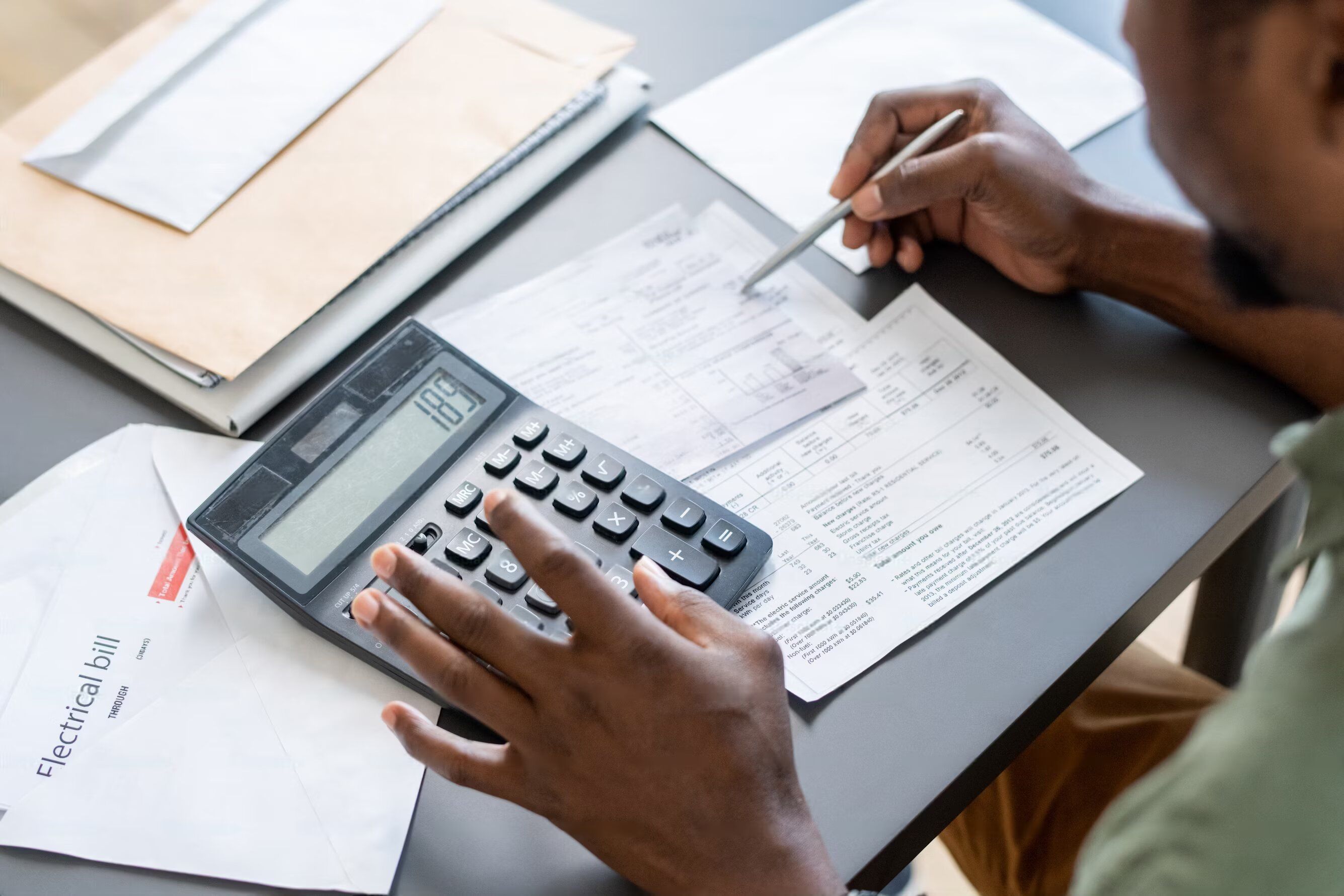  A man at his desk is engaged in tax preparation, utilizing a calculator and reviewing various bills.
