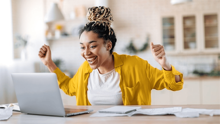 "African lady smiling excitedly at her laptop on the desk, wearing a yellow skirt