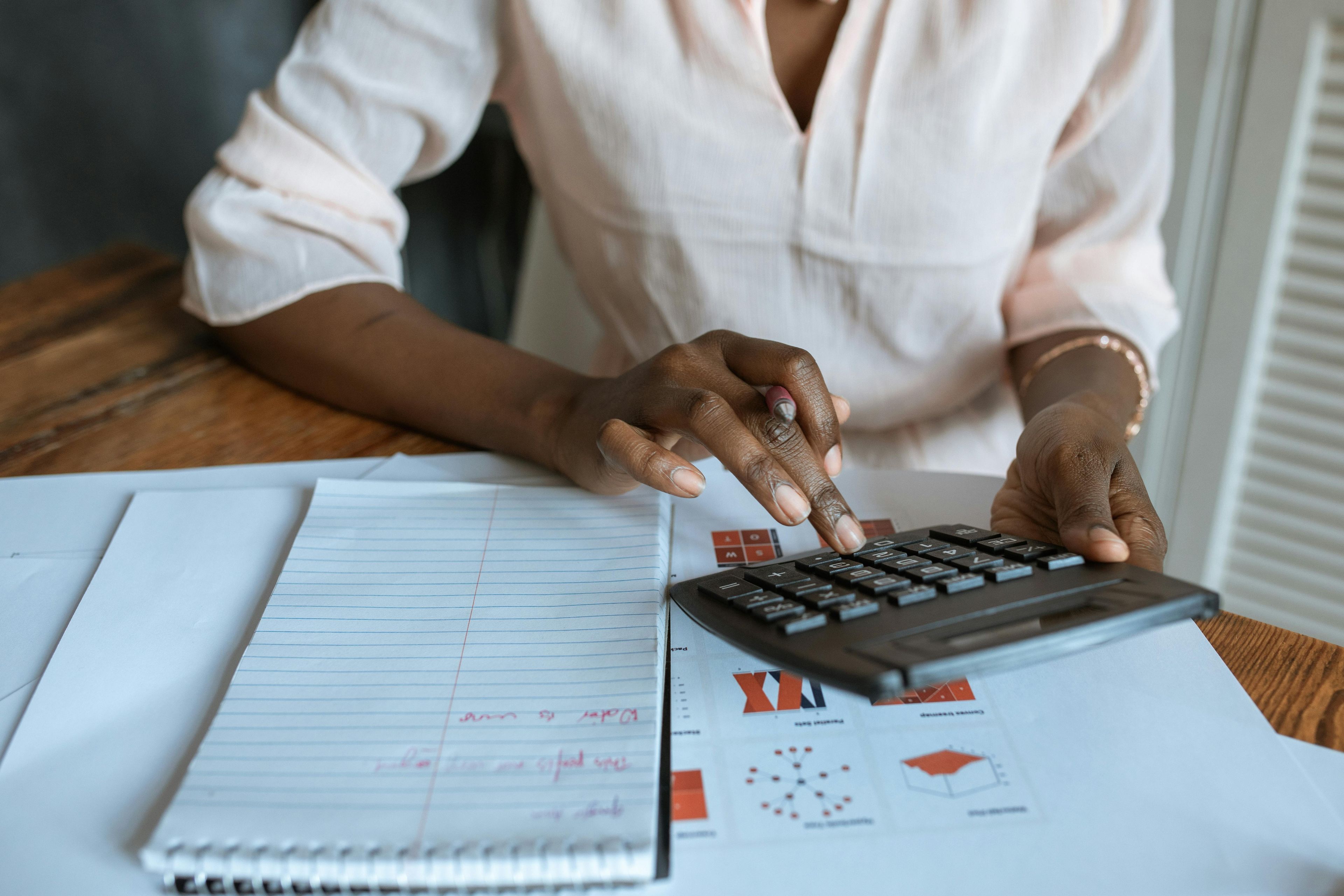 A woman focused on a calculator, working on her business books with financial documents spread out before her