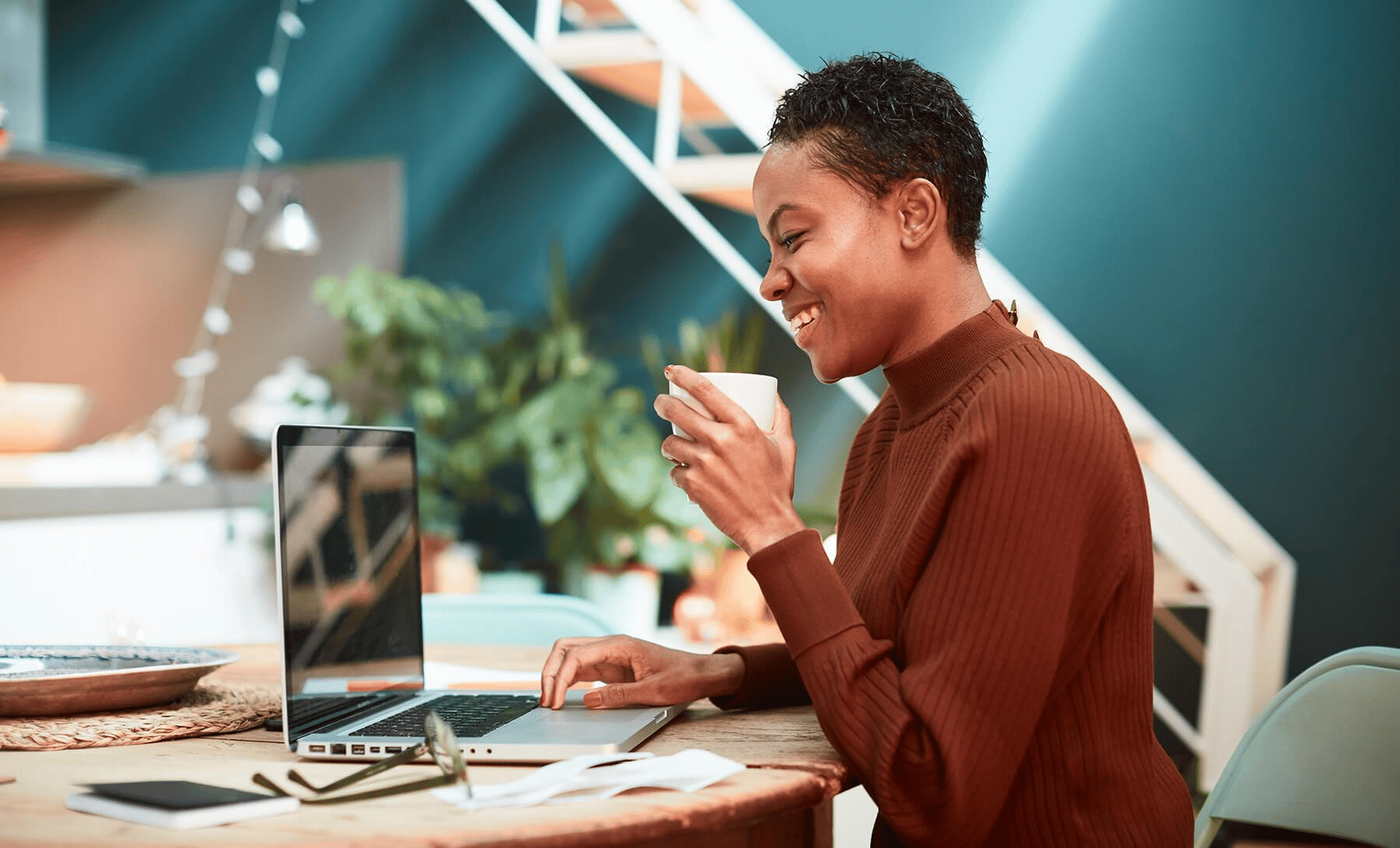 "Confident African woman enjoying coffee while working on a laptop, symbolizing productivity and professionalism.