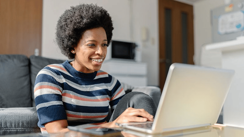 Smiling African woman working from home on a laptop, representing remote work and productivity.